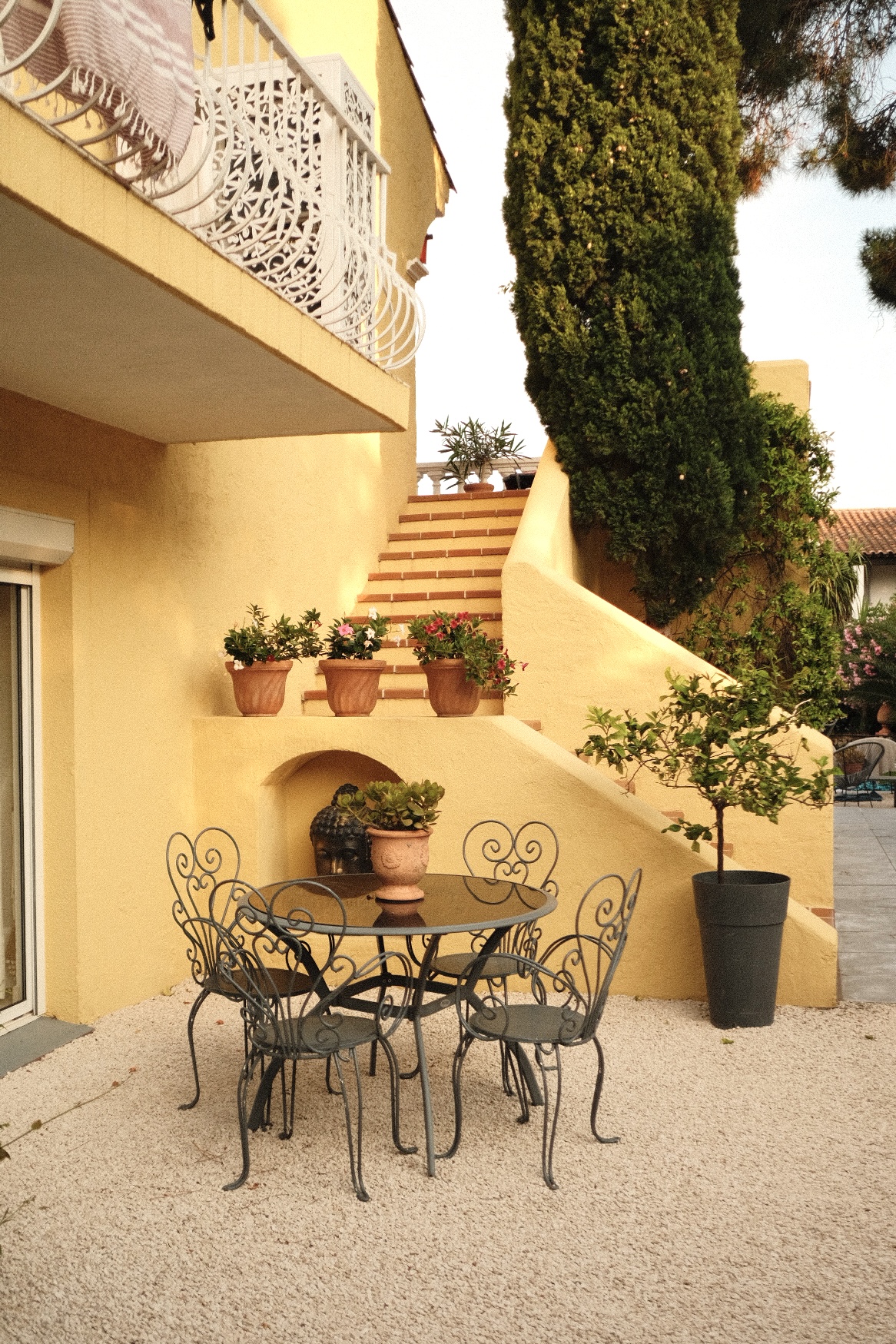 Yellow villa courtyard with wrought-iron table and terracotta pots